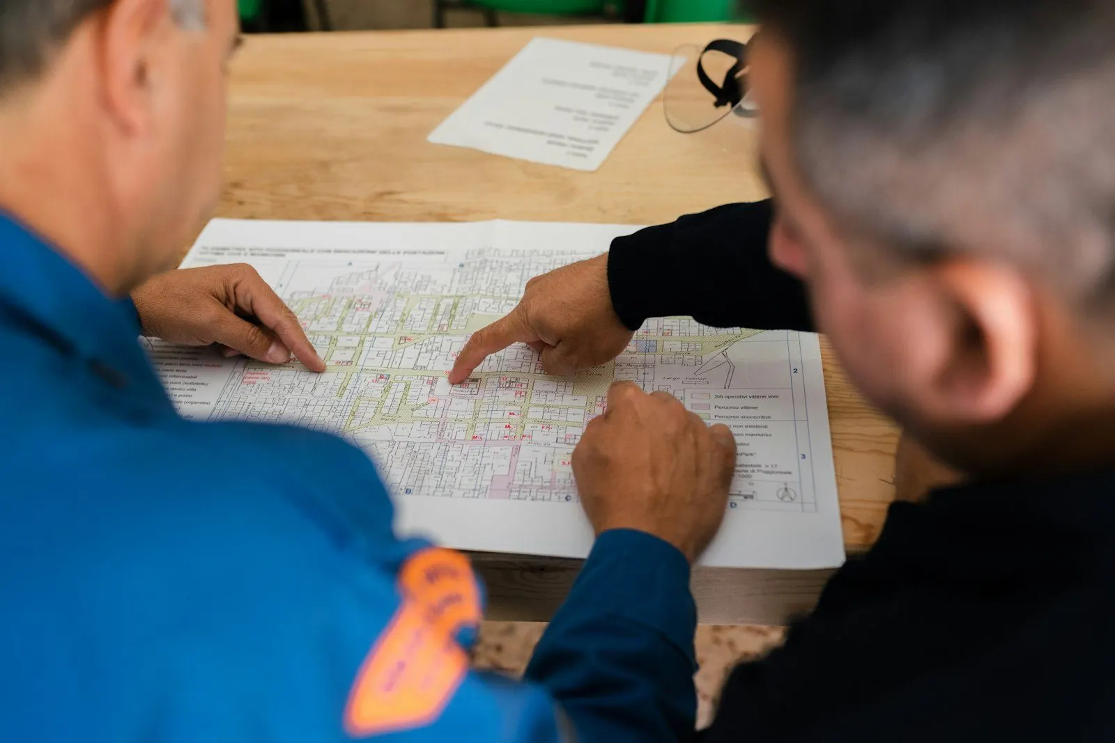 Dos técnicos con uniforme señalando un plano sobre la mesa